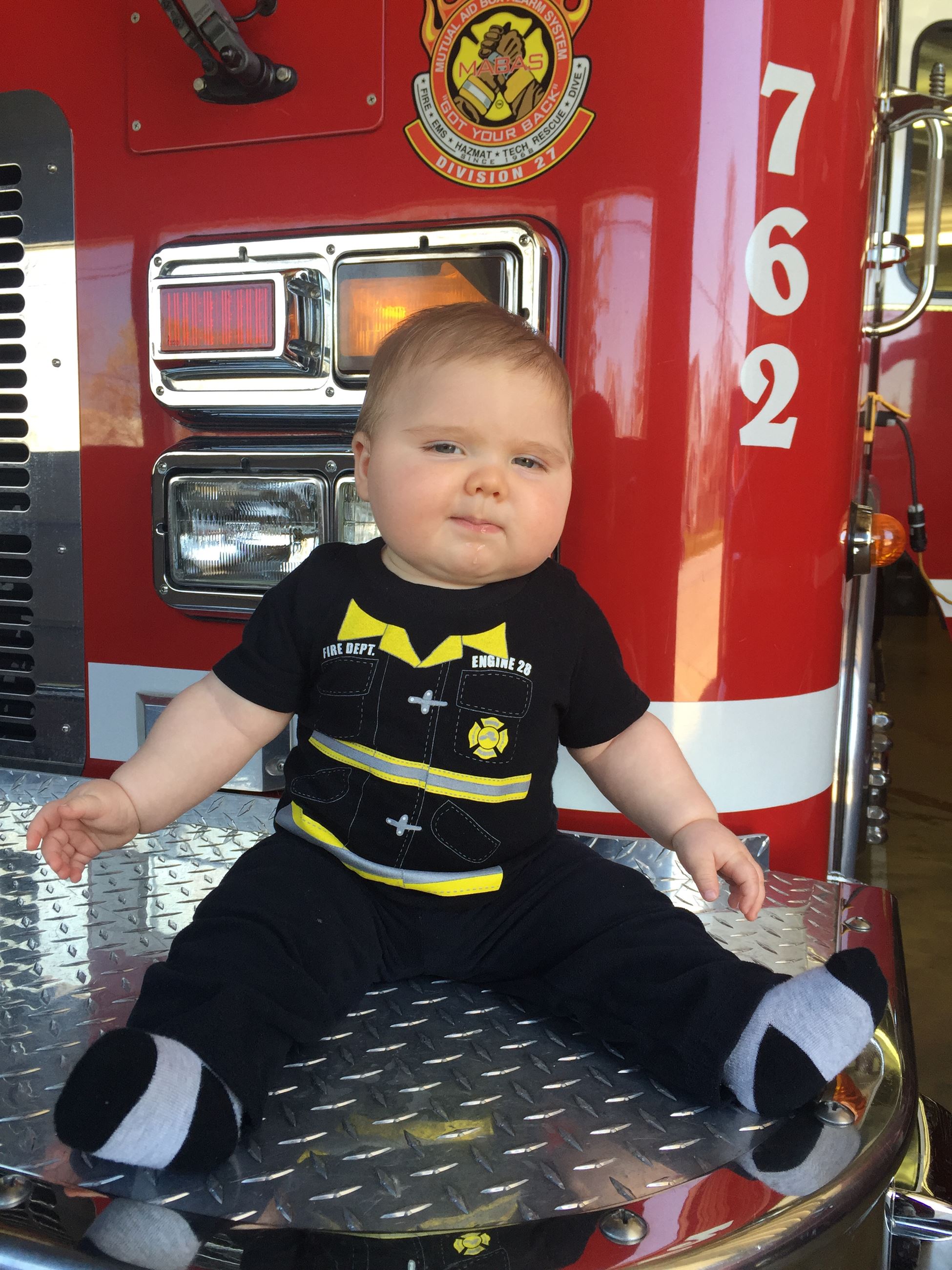 Baby dressed in a onesie that looks like a firefighter's uniform